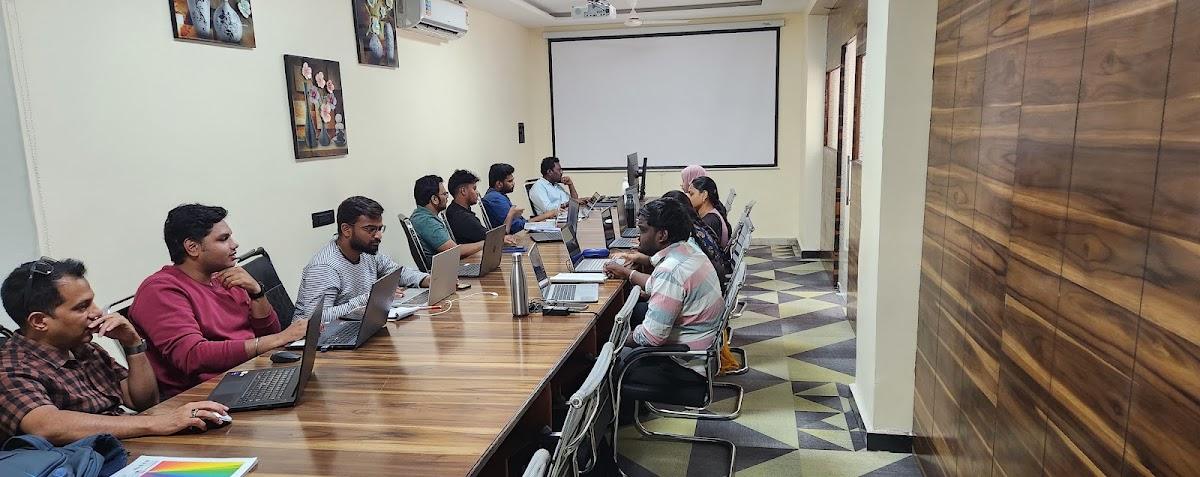Students working on laptops at a long table in the Ameerpet training room, facing a projector screen